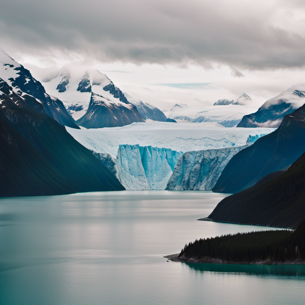 An image showcasing a majestic Alaskan landscape: a colossal glacier towering over a serene fjord, surrounded by snow-capped mountains that stretch endlessly into the distance, illustrating the vastness and grandeur of an Alaskan cruise